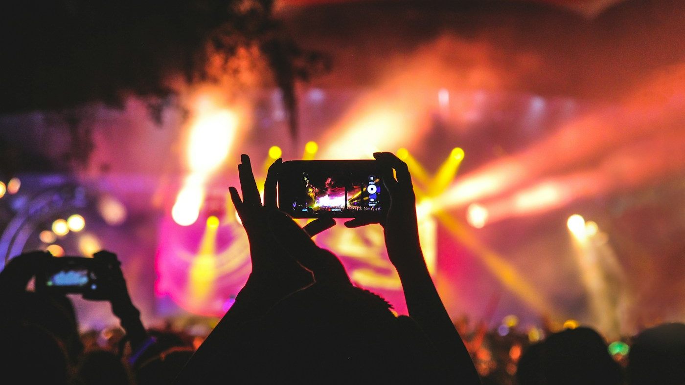 Silhouetted hands holding up a phone to record a concert under stage lights