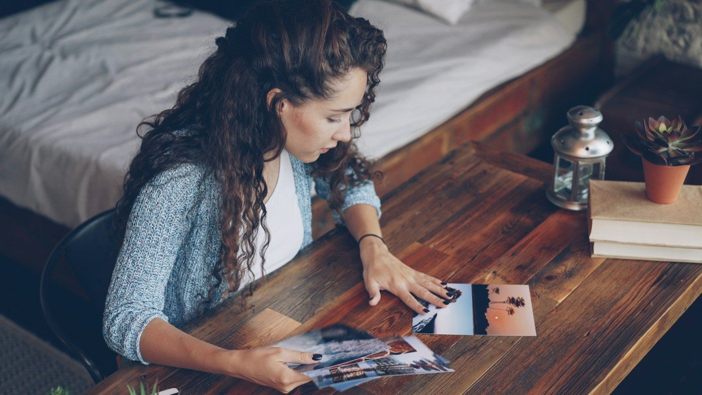 Woman at a wooden table sorting through printed photos from a beach trip