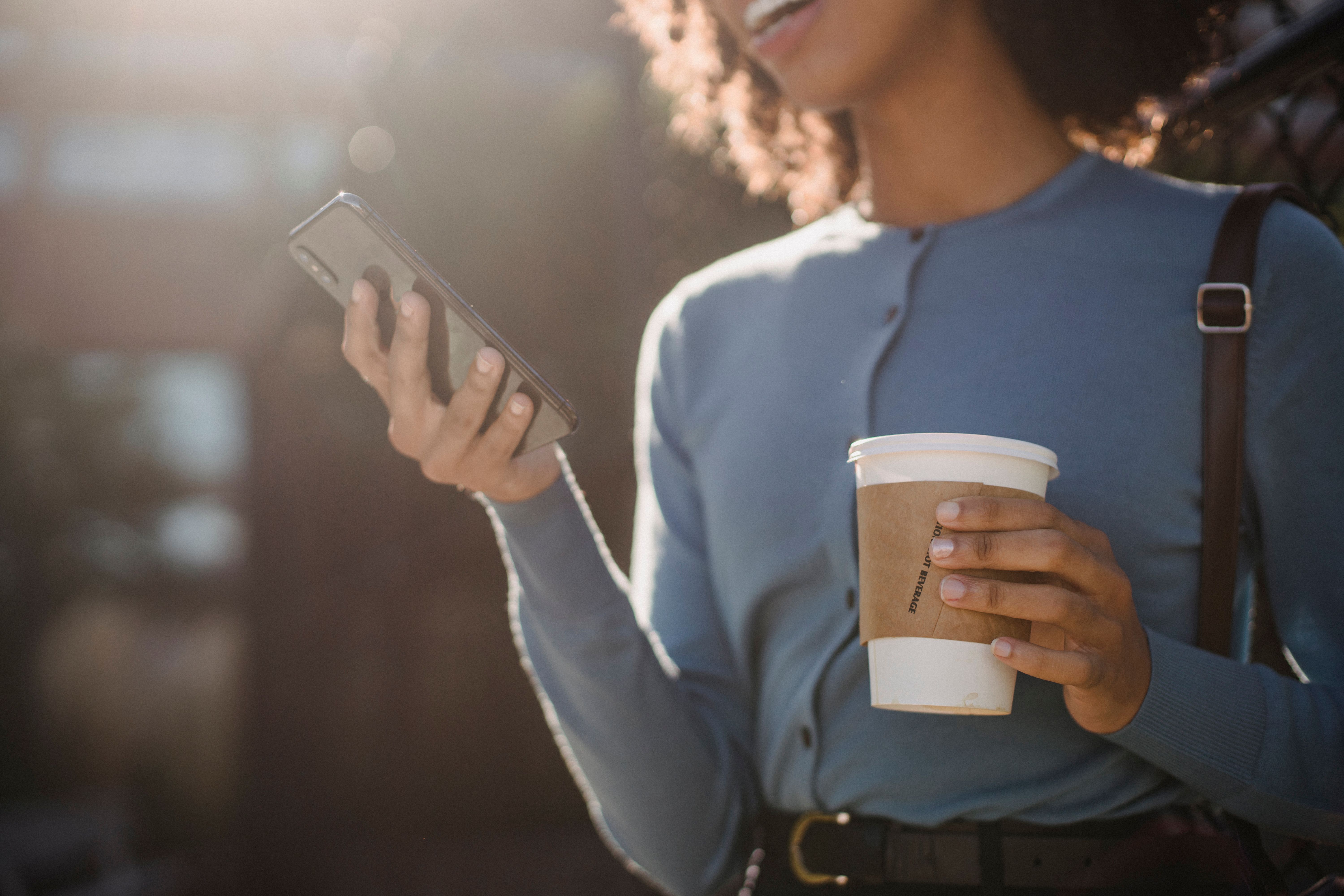 Woman holding a cup while browsing photos on her phone